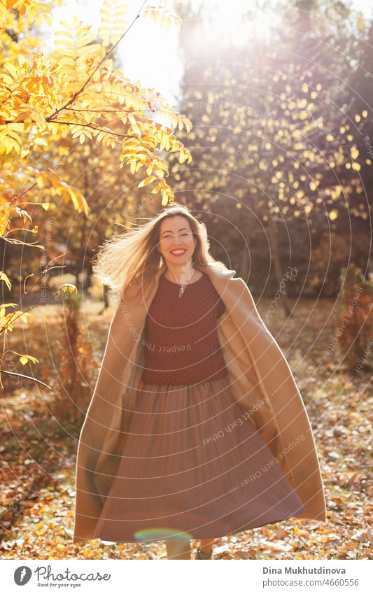 Schöne Frau in beigem Mantel, weinrotem Pullover, braunem Rock und rotem Lippenstift Make-up, zu Fuß im Herbst Park. Porträt eines Mädchens im Herbst Natur mit gelbem Laub.