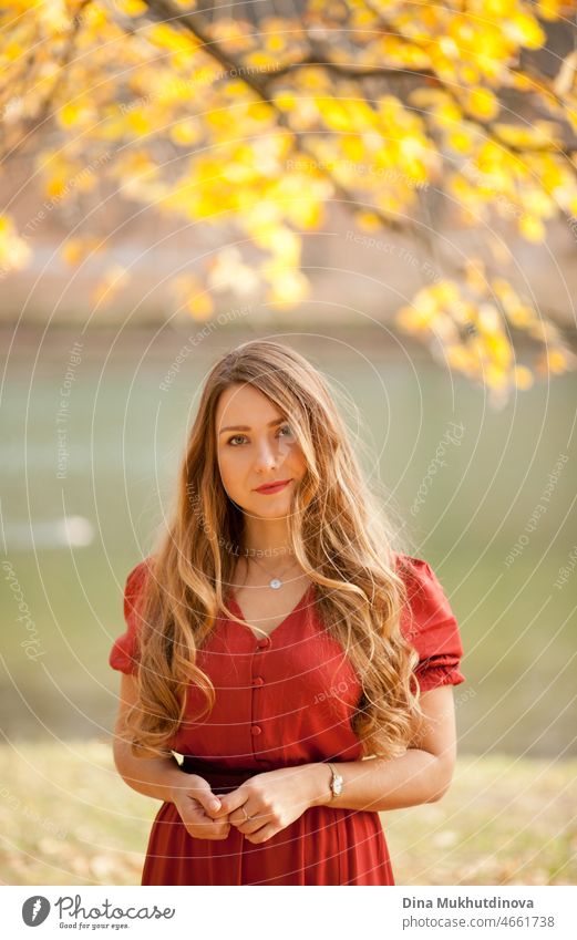 schöne Frau mit langen in rotem Kleid zu Fuß in den Wald am See unter Bäumen. Romantischer Spaziergang im Wald im Herbst Natur auf Herbstblätter. Erwachsener