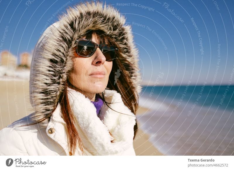 Glückliche Frau in weißer Jacke und Sonnenbrille an einem sonnigen Wintertag am Strand 45-50 Jahre außerhalb Emotion Dame 40s brünett sorgenfrei Ausdruck