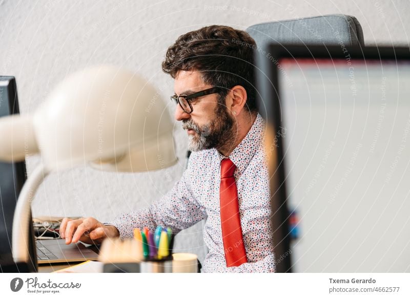 Geschäftsmann mittleren Alters mit Bart und Brille, der sich auf seine Arbeit vor seinem Computer konzentriert Konzentration Büro Designer Atelier Vollbart