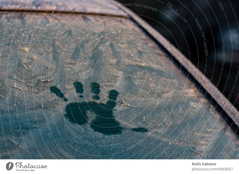 Handabdruck auf der verschneiten und vereisten Windschutzscheibe eines Autos. Morgensonnenaufgang Licht abstrakt Hintergrund schön blau Nahaufnahme kalt Konzept