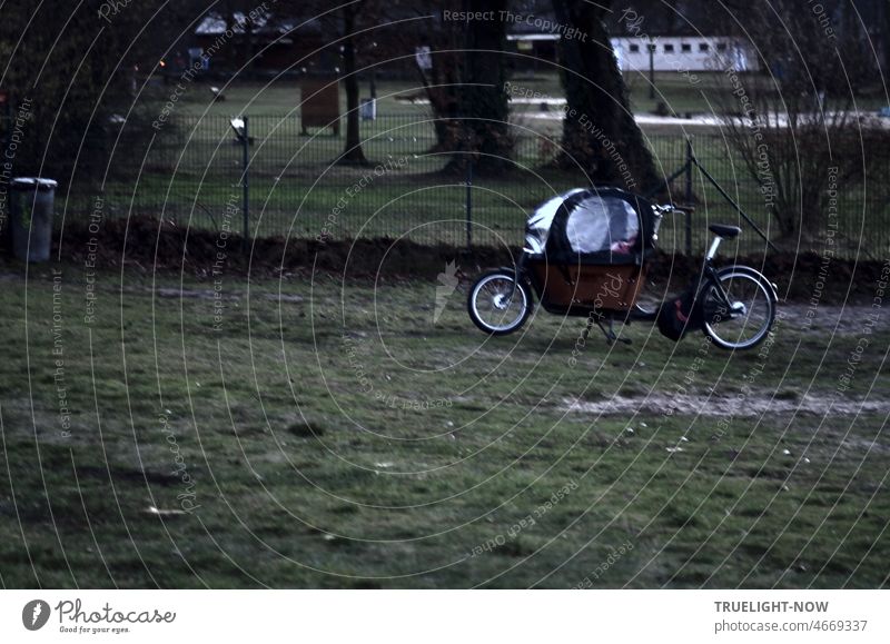 Ein Lastenfahrrad, eine moderne Fahrrad Kinder Rikscha mit durchsichtiger Schutzhaube für Fahrten bei Wind und Wetter parkt auf einer Wiese am Havel Strandbad in Babelsberg