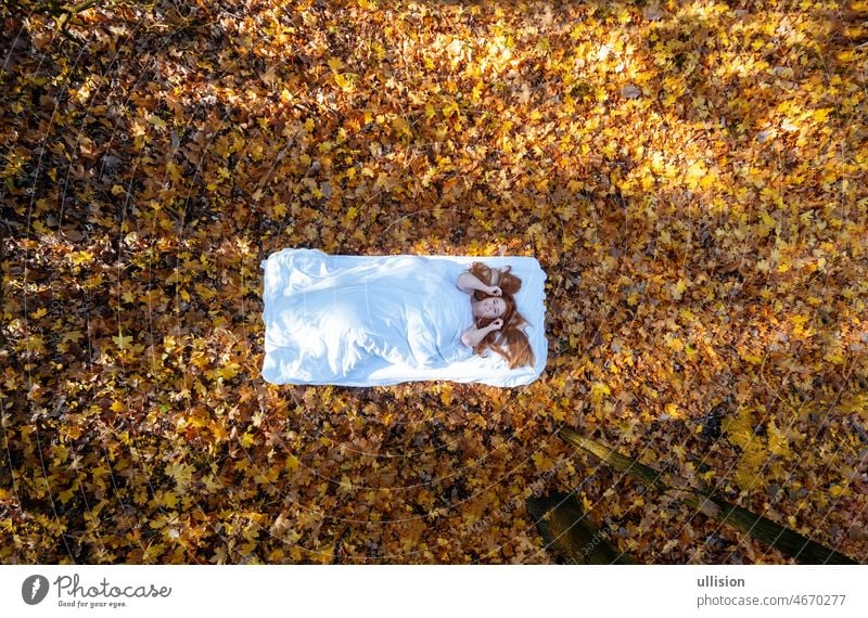 Draufsicht von oben auf eine schöne sexy rothaarige niedliche reife Frau, mit gelben, orangefarbenen Ahornblättern im Bett, mit glücklichem Lächeln im Gesicht. copy space