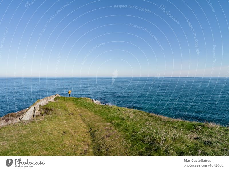 Küstenlandschaft und Mädchen in gelbem Kapuzenmantel, das aufs Meer schaut und spazieren geht. Raum kopieren. Landschaft MEER Himmel Küstenlinie Frau Person