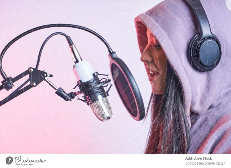 Frau singt im Studio ins Mikrofon Sänger singen Gesang Sängerin Kopfhörer Aufzeichnen Musik Stimme Klang Kapuzenpulli lässig Pop-Filter feminin Vorschein jung