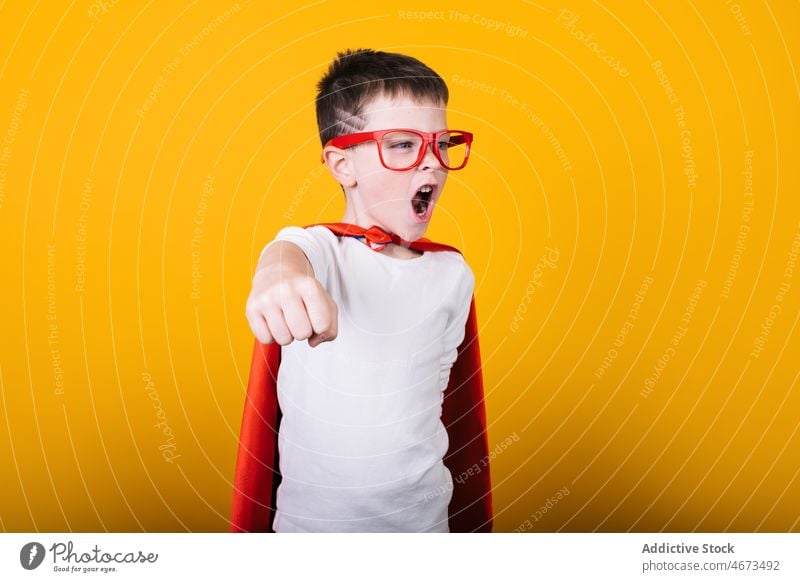 Verspielter Junge in Superhelden-Uniform, der so tut, als würde er fliegen Kind Flug Fliege die Faust ballen schreien Tracht Porträt Atelier Kraft Mut Held