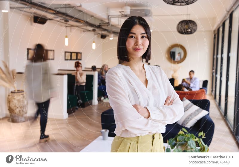 Porträt einer selbstbewussten chinesischen Frau mittleren Alters, die in die Kamera schaut und lächelt, in einem Coworking Space Internationaler Frauentag