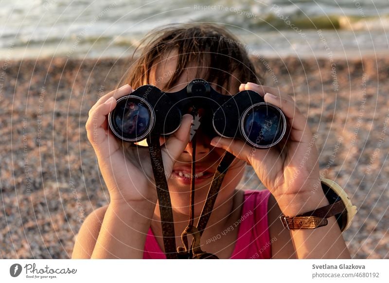 Gebräuntes Kleinkind mit braunen Haaren am Strand im Sommer schaut durch ein Fernglas Sonnenuntergang Kind niedlich Mädchen Glück Feiertag MEER Lächeln reisen