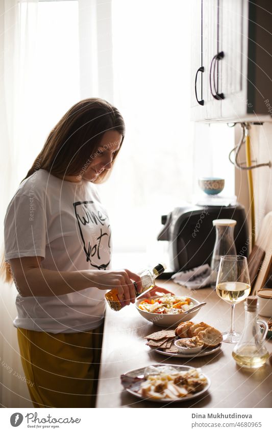 Frau kocht Abendessen zu Hause und trinkt Weißwein. Junge Frau kocht Salat zum Mittag- oder Abendessen und bereitet Vorspeisen zu.  Frau in der Küche, beim Kochen. Essen und Trinken.