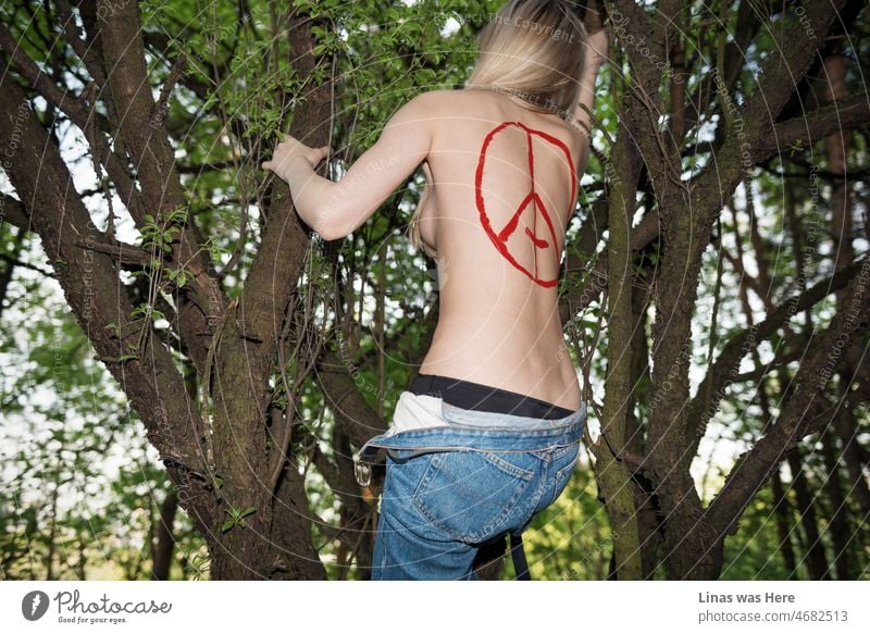 Solch ein lustvoller Anblick in diesem tiefen Wald. Ein oben ohne blondes Mädchen klettert auf einen Baum mit einem Teufelszeichen auf ihrem sexy Rücken. Blaue Jeans und schwarze Unterwäsche ist alles, was sie trägt.