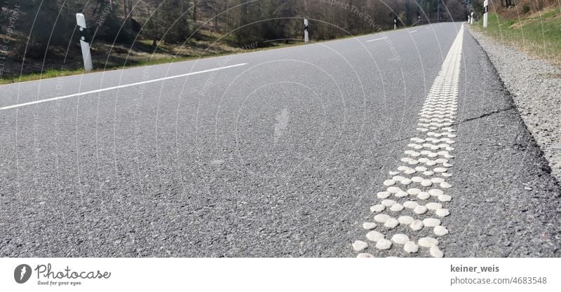 Asphaltierte Straße mit genoppter akustischer Fahrbahnmarkierung. Ruhige Landstraße im Spessart mit Randstreifen Pfosten Linie Noppen Randsteifen grau