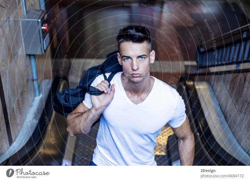 Junger weißer Mann, der auf einer Rolltreppe am Flughafen nach oben fährt. Stehen eine Person U-Bahn Erwachsener horizontal Tasche Passagier Pendler modisch