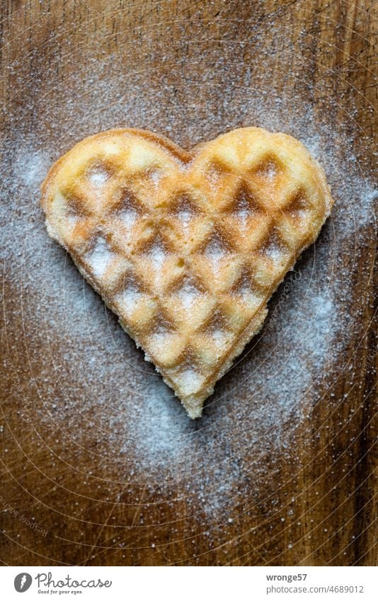 Selbst gebackenes, leckeres mit Puderzucker bestreutes Waffelherz liegt auf einem Holzbrettchen selbst gebacken selber gebacken selbstgebacken selbergebacken