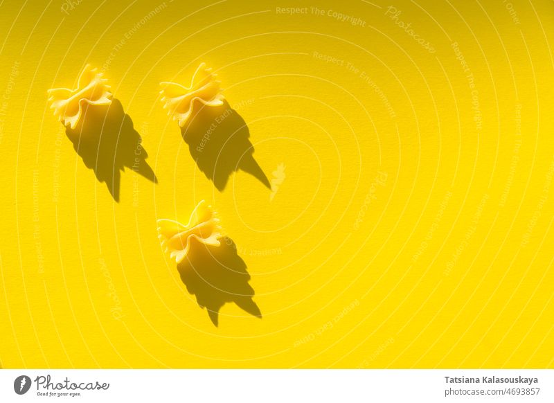 Drei Stücke von Farfalle-Teig auf gelbem Hintergrund Lebensmittel ungekocht roh Spätzle drei Italienisch Bestandteil Diät Ernährung Weizen Gesundheit