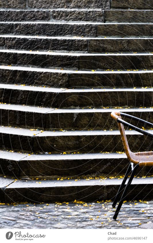 Teekesselchen/ Treppenstuhl-Stuhltreppe.  Rattan Stuhl vor Steintreppe Stufe Stufen Pflaster schwarz dunkel Kante Ecke Rohrstuhl Laub öffentlicher Raum Möbel