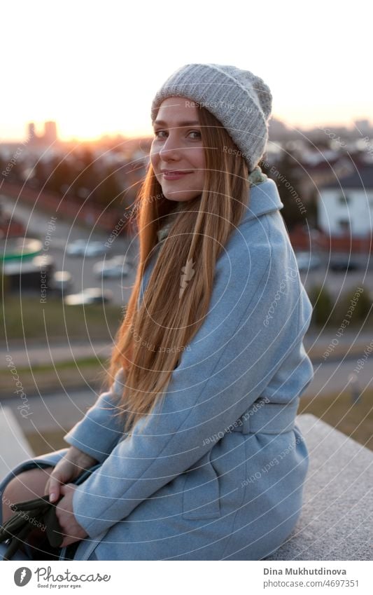 Frau in stilvollem blauen Mantel bei Sonnenuntergang. Weibliche Reise. Schöne attraktive junge Frau zu Fuß auf der Straße bei Sonnenuntergang oder Sonnenaufgang früh am Morgen in der Nähe der modernen Architektur Gebäude in der Stadt. Casual candid Lebensstil.