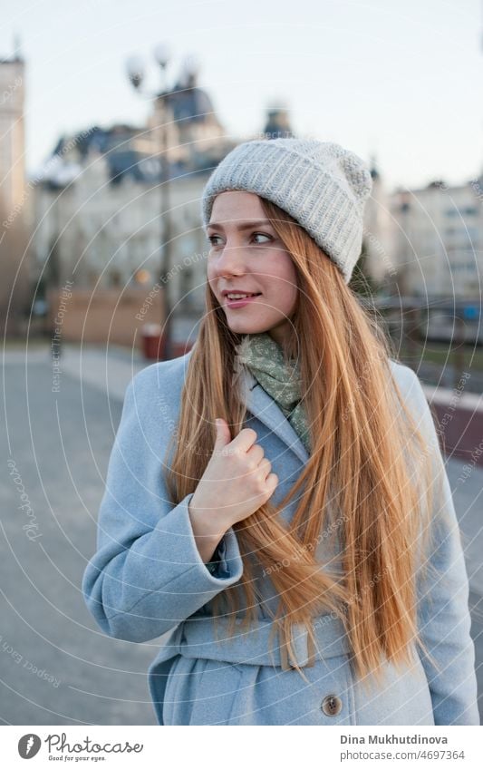 Frau in stilvollem blauen Mantel bei Sonnenuntergang. Weibliche Reise. Schöne attraktive junge Frau zu Fuß auf der Straße bei Sonnenuntergang oder Sonnenaufgang früh am Morgen in der Nähe der modernen Architektur Gebäude in der Stadt. Casual candid Lebensstil.