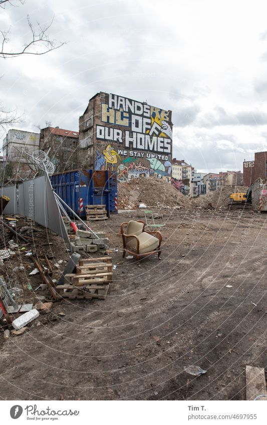 Ein leerer Platz besetzt mit einem alten Sessel . Im Hintergrund ein besetztes Haus mit Graffiti. Berlin Hands homes Winter Ruine Menschenleer Tag Farbfoto Wand