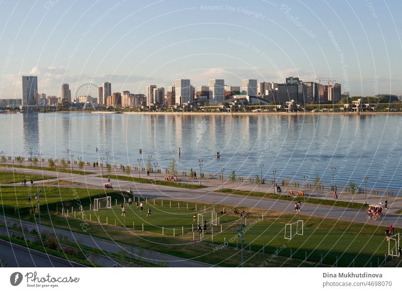 Skyline der Stadt bei Sonnenuntergang zur blauen Stunde. Stadtansicht reflektiert in Fluss Wasser und Fußballfelder. Urban Stadtbild Reflexion im Wasser und moderne Architektur. Vertikale städtischen Sommer Hintergrund.