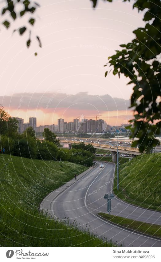 Stadtlandschaft mit einer leeren Straße und Gebäuden bei Sonnenuntergang und grünem Gras und Baumblätter. Sommer in der Stadt vertikalen Hintergrund. Warme Sommernächte städtischen Hintergrund.