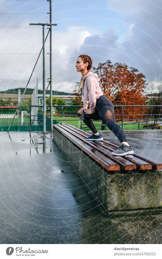 Junge Sportlerin streckt die Beine im Freien strecken auf einer Bank Boxerflechten Frau Athlet Körper Aufwärmen Training geduckt trainiert. regnerisch Morgen