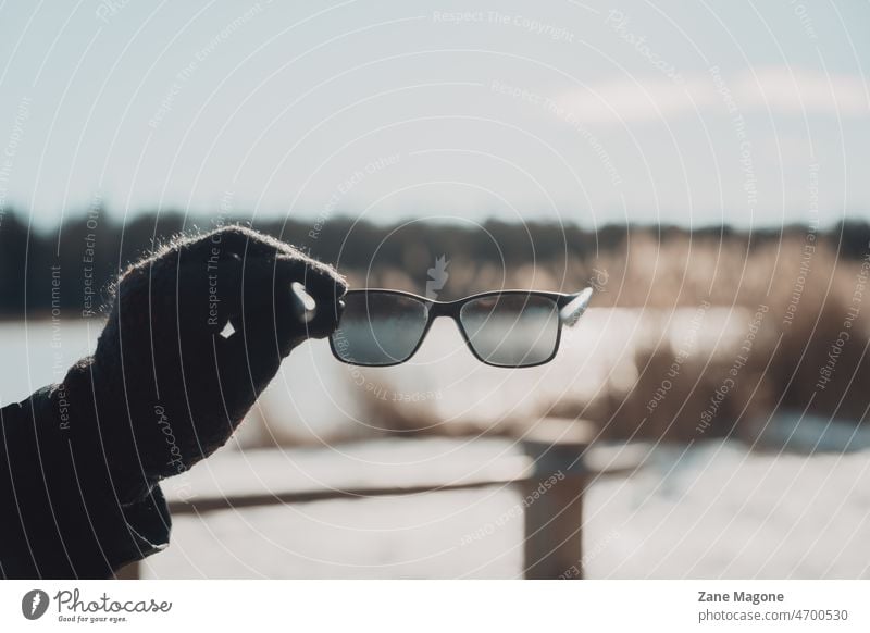 Hand hält Sonnenbrille in sonnigen Tag Frühling hell Licht Wintersonne Frühlingssonne Filter Blick gepolt Landschaft Saisonwechsel helle Sonne Sonnenlicht