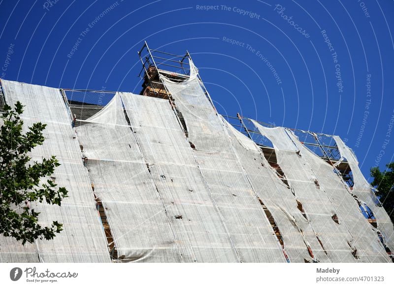 Baugerüst mit zerfleddertem Sicherheitsnetz bei der Sanierung der Fassade eines großen Altbau vor blauem Himmel bei Sonnenschein im Stadtteil Sachsenhausen in Frankfurt am Main in Hessen