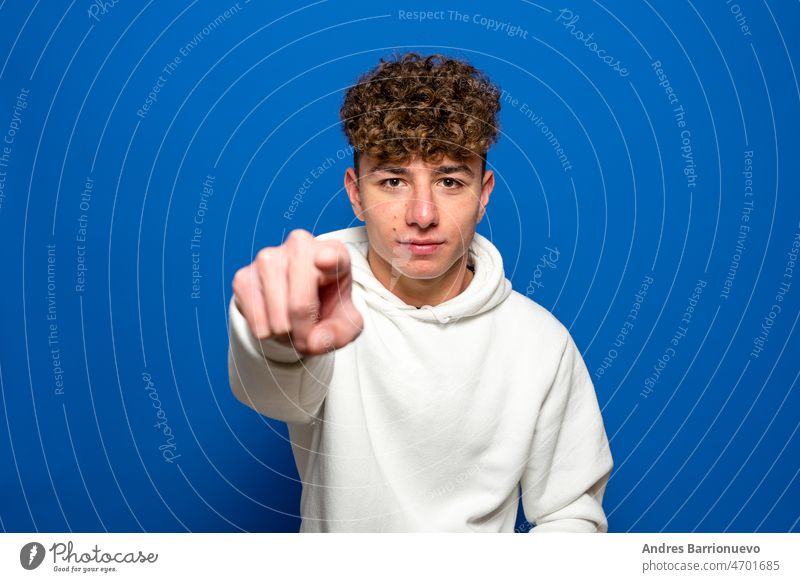 Junger gutaussehender dunkelhaariger Mann mit lockigem Haar, der ein weißes Sweatshirt auf blauem Hintergrund trägt und verärgert und frustriert in die Kamera zeigt, wütend und zornig auf Sie.