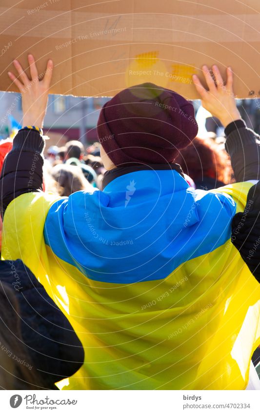 Friedensdemonstration gegen den von Putin begonnenen Angriffskrieg gegen die Ukraine. Demonstrantin in den Landesfarben der Ukraine welche ein Schild hoch hällt. Rückansicht