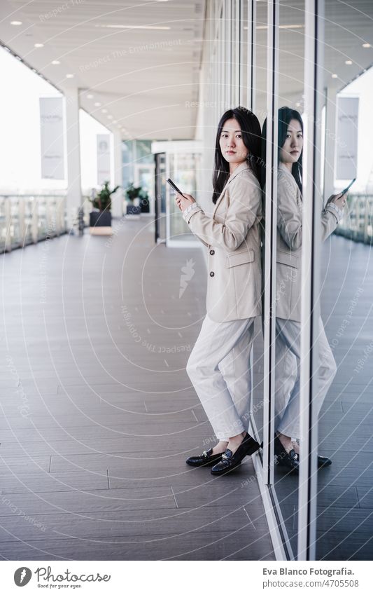 Porträt einer schönen chinesischen Geschäftsfrau, die in einem Bürogebäude ein Mobiltelefon benutzt. Technik Chinesisch asiatisch Frau Laptop