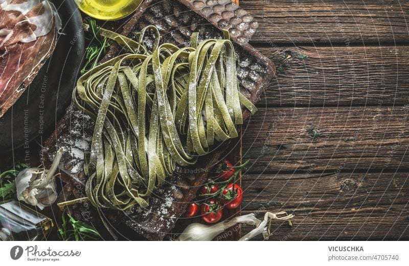 Nahaufnahme von selbstgemachten grünen Tagliatelle-Nudeln Mehl abschließen rustikal Tablett hölzern Küche Tisch Tomaten Olivenöl Knoblauch Schinken traditionell