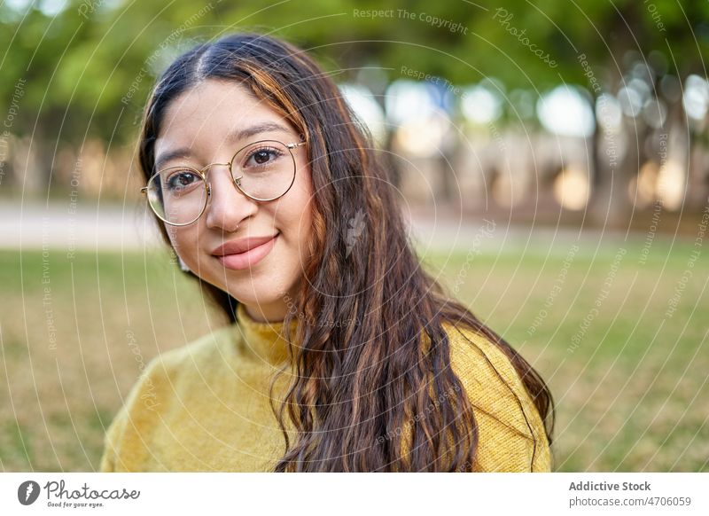 Positive Frau auf dem Rasen sitzend Park feminin Vorschein Stil Lächeln Sommer jung Baum Brille Dame angenehm Pflanze lange Haare Jugend schön Charme Umwelt