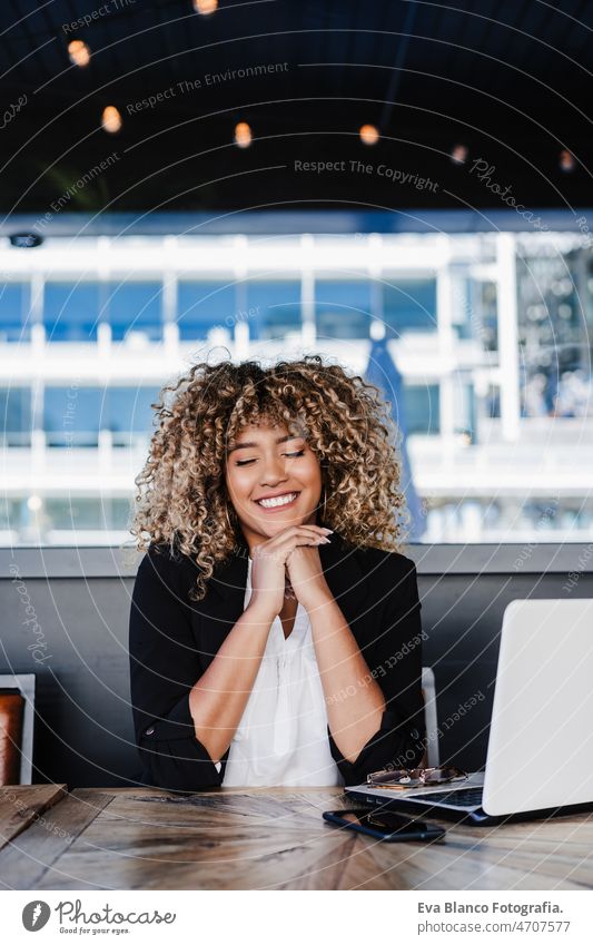 Lächelnde hispanische afroamerikanische Geschäftsfrau in einem Café, die an einem Laptop und einem Mobiltelefon arbeitet. Computer Afro-Look Frau Business