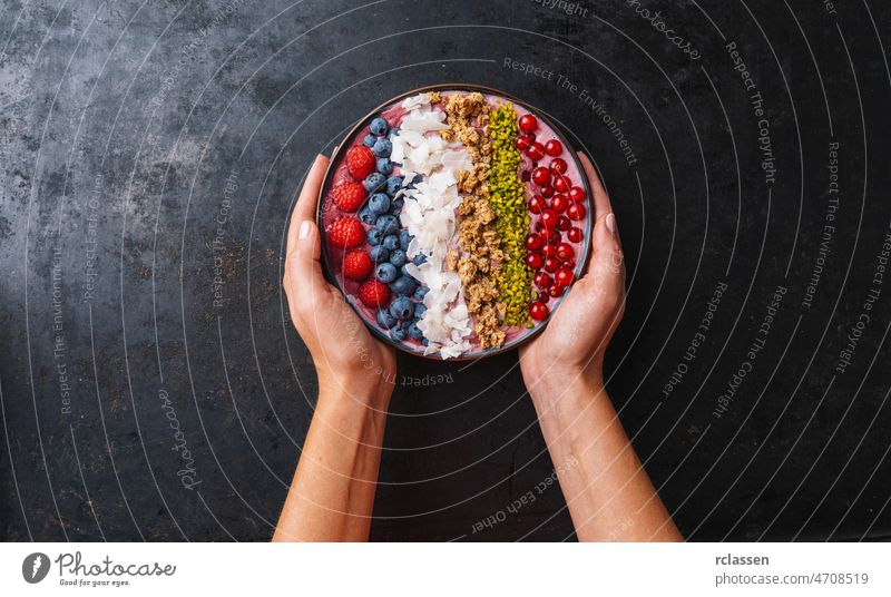 Eine Frau hält eine gesunde Frühstücksschüssel mit einem Blaubeer-Smoothie mit Himbeeren, Blaubeeren, Kokosnuss, Nüssen und Johannisbeeren Schalen & Schüsseln