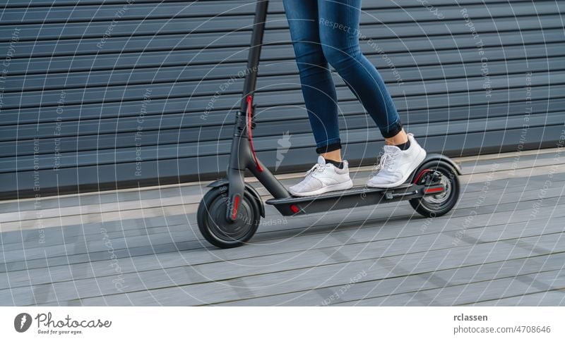 Nahaufnahme einer Frau auf einem schwarzen Elektroroller in einer Stadtlandschaft, Bewegungsunschärfe Tretroller Großstadt Kick E-Roller Stadtzentrum Turnschuh