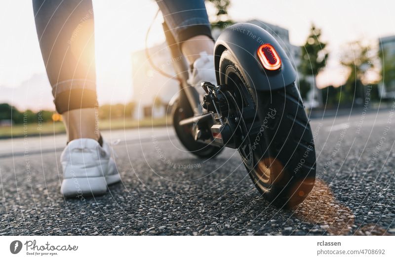 junge Frau auf dem Elektroroller auf der Straße bei Sonnenuntergang Tretroller Großstadt Kick E-Roller Stadtzentrum Turnschuh Fahrrad Laufwerk Aktivität