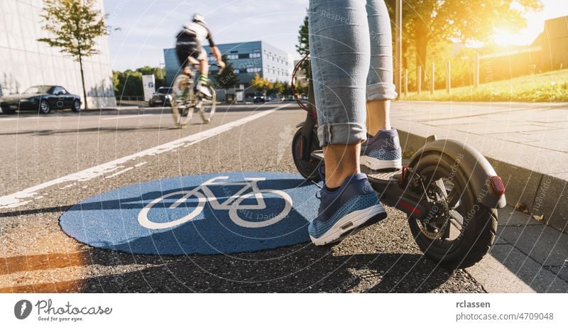 Close up von Frau beginnen, einen elektrischen Roller oder Kick-Scooter bei Stadtbild auf einem Fahrrad Wegweiser zu fahren Tretroller aktiv Großstadt E-Roller