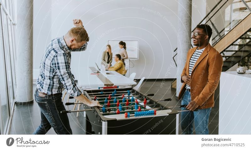 Junge lässige multiethnische Geschäftsleute spielen Tischfußball und entspannen sich im Büro Geschäftsfrau Geschäftsmann Kollegen Erwachsener Spiel