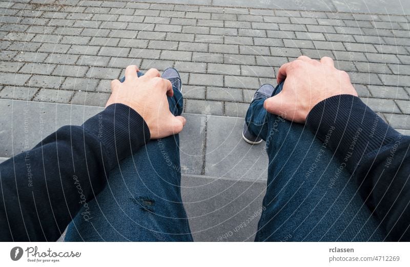 Mann sitzt auf einem Bordstein und wartet nervös auf jemanden, Point of view shot pov Menschen Lifestyle Punkt Ansicht Sommer Weg Kaukasier Nahaufnahme jung