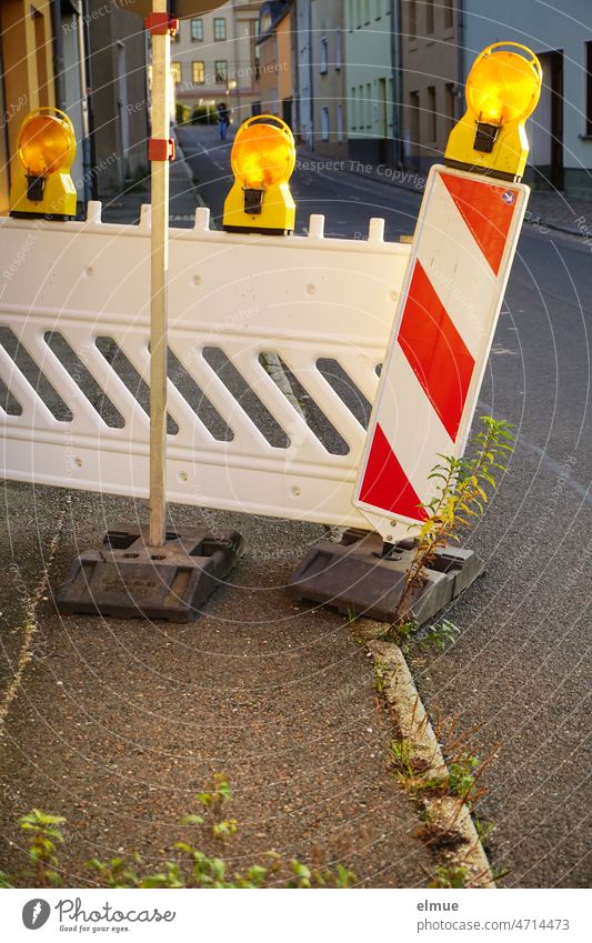 Verkehrsbake mit Bakenleuchten quer über dem asphaltierten Fußweg in der Gasse einer Kleinstadt / Absperrung Verkehrsbaken Baustelle Warnbake Absperrgitter