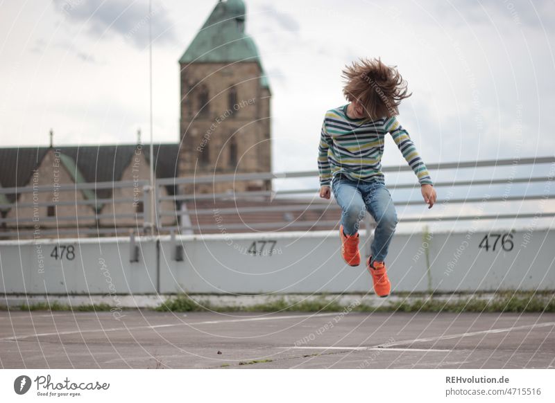 Kind springt in die Luft Spielen urban Stadt Parkplatz Beton Aktion Außenaufnahme Fitness leer grau Bewegung bewegen Dynamik draußen hüpfen sprung springen hoch