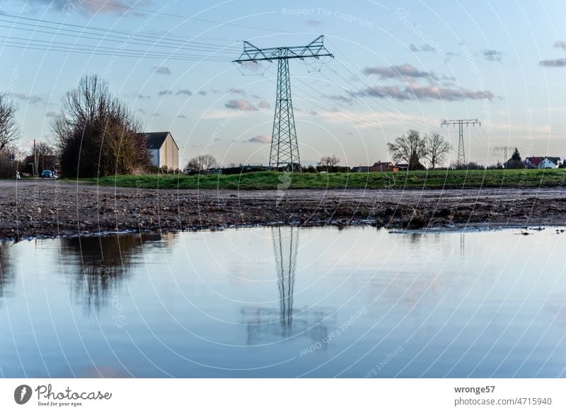 Hochspannungsleitung am Dorfrand spiegelt sich in einer Regenpfütze Hochspannungsleitungen Hochspannungsmasten Freileitung Spiegelung im Wasser Pfütze