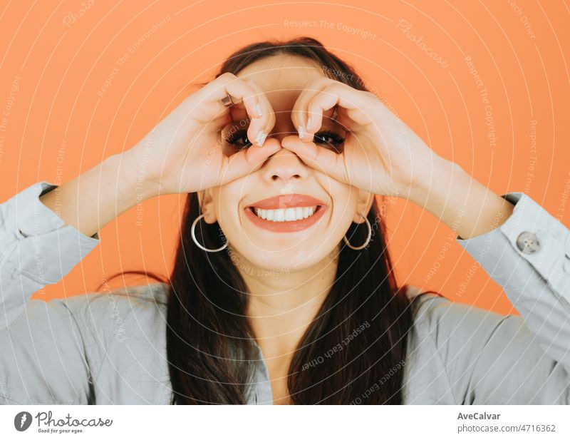 Junge afrikanische Frau mit seinen Händen als Fernglas lächelnd zur Kamera auf der Suche nach etwas posiert isoliert über orange Farbe Wand Hintergrund. Tägliche Ausdrücke mit Kopie Raum im Studio.