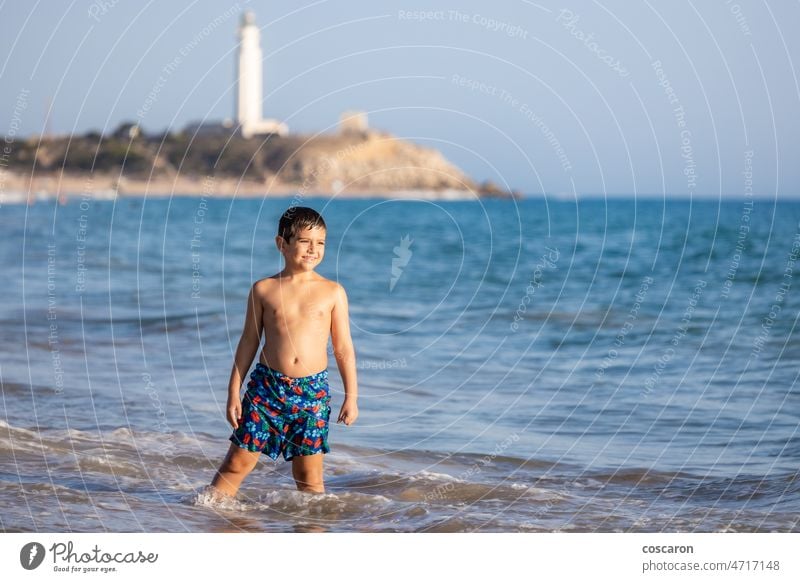 Lustiges Kind genießt das Wasser des Ozeans mit einem Leuchtturm Hintergrund Barbate Strand Junge Cadiz Küste Küstenlinie Staatsstrand El Matador genießen Abend