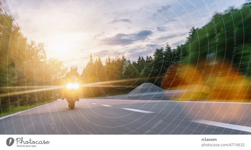 motorrad auf der waldstraße fahrend mit bewegungsgeschwindigkeit. fahrt auf der leeren straße auf einer motorradtour bei sonnenuntergang. copyspace für ihren individuellen text.