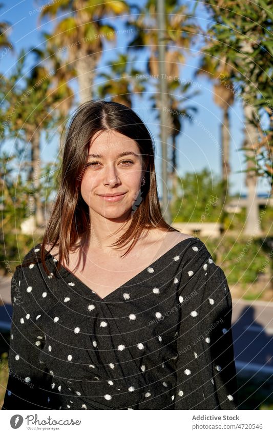 Fröhliche Frau auf sonniger Straße stehend Vorschein Stil feminin Mode Outfit Freizeit Kleidungsstück Bekleidung heiter Baum Sommer jung positiv Optimist Dame