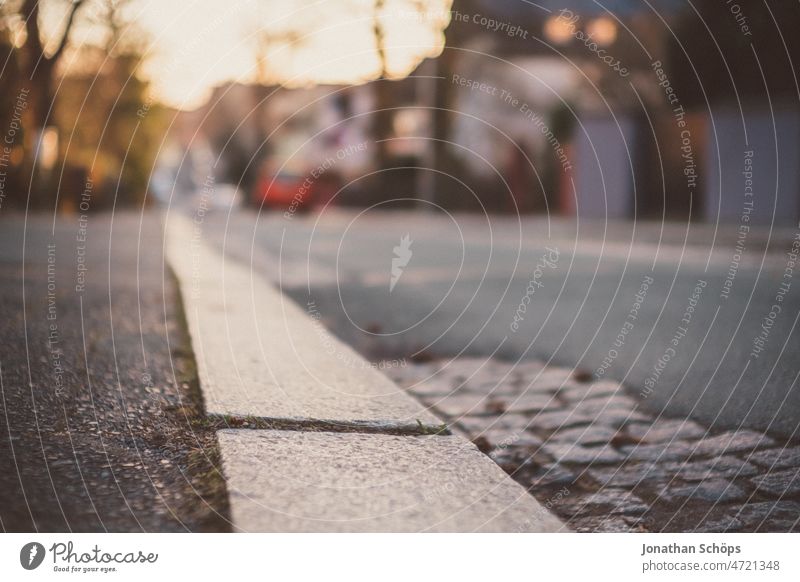 Bordsteinkante auf einer Straße bei Abendsonne Fußweg Bürgersteig Gehweg sonnig Winter Straßenrand Straßenbelag urban leer Asphalt Kopfsteinpflaster