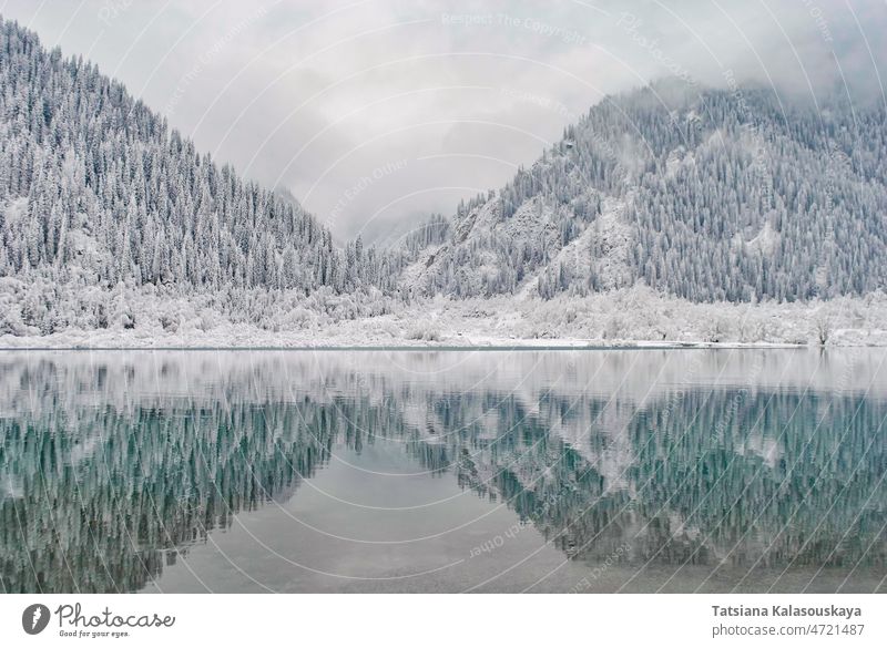 Bergsee im Winter. Die schneebedeckten Berge spiegeln sich im Wasser kalt gefroren kühl Kälte Winterzeit Frost Einfrieren Raureif ob Hügel Berge u. Gebirge