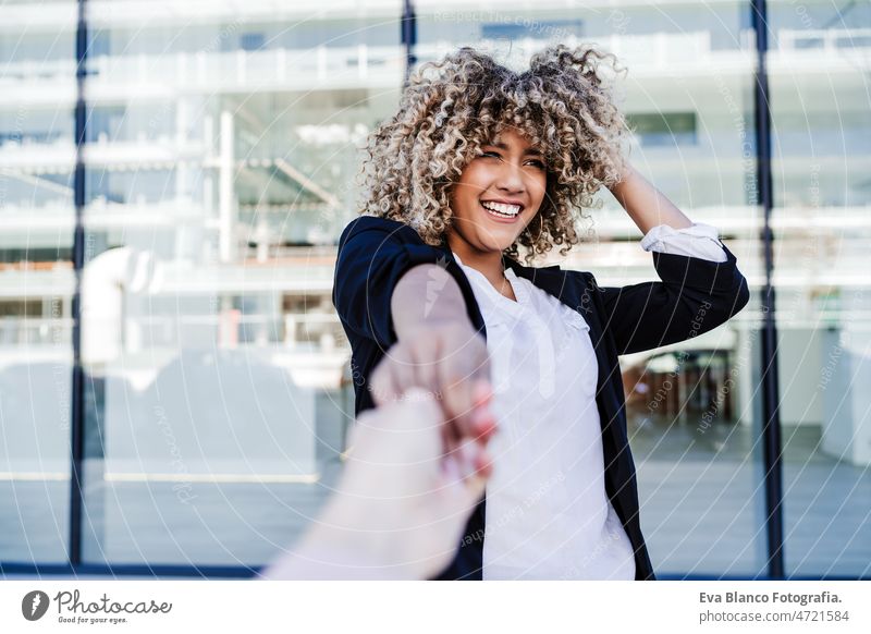 schöne lachende Geschäftsfrau in der Stadt hält Hand mit Freund. Gebäude Hintergrund Glück Händchen haltend Großstadt Lachen Freunde Afro-Look hispanisch Handy