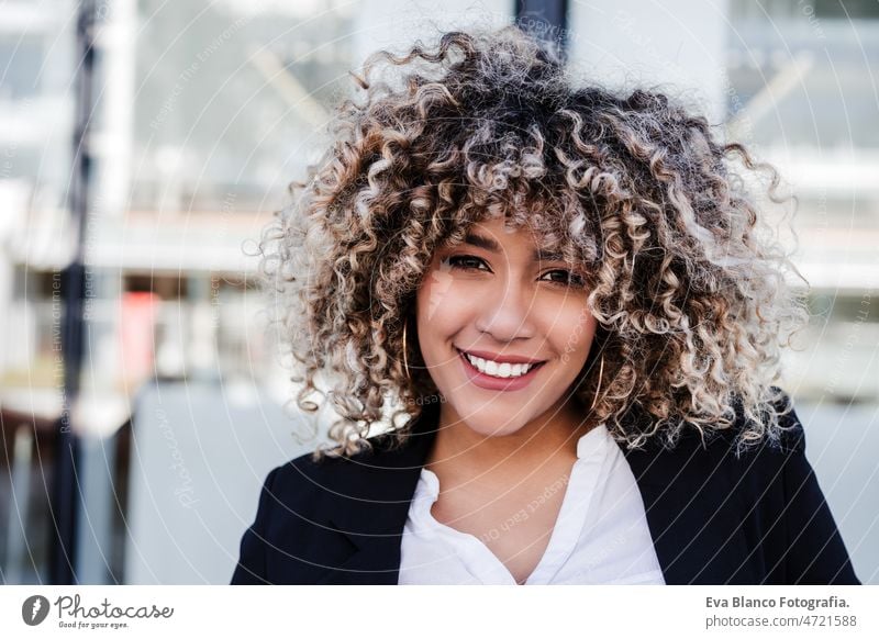 Porträt einer selbstbewussten hispanischen Geschäftsfrau in der Stadt. Gebäude Hintergrund Afro-Look Handy Großstadt Wolkenkratzer Business jung krause Haare